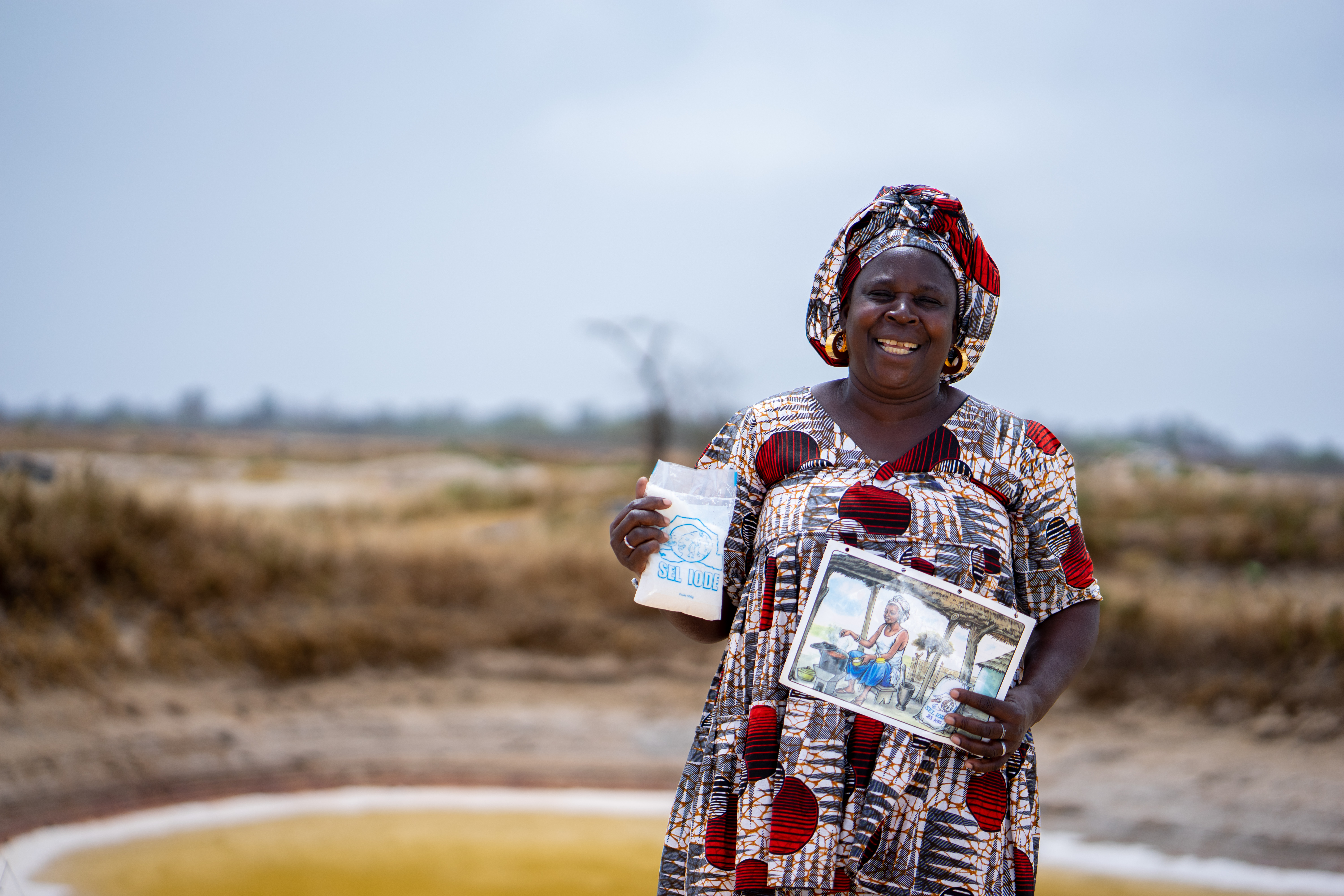 A woman holds up a phamplet on salt iodization and smiles at the camera.