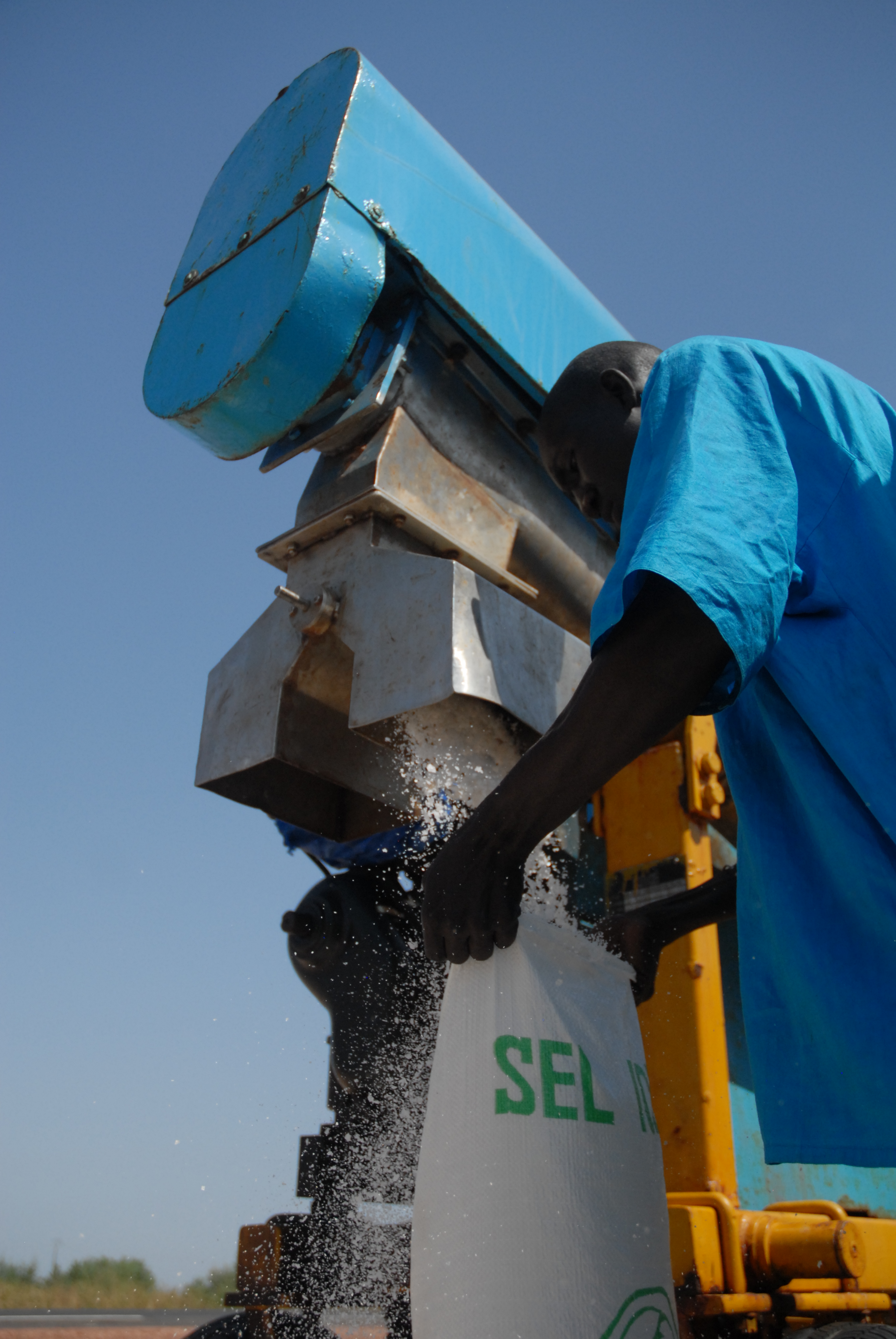 A man holds a bag under a machine outside that is filling it with iodized salt.