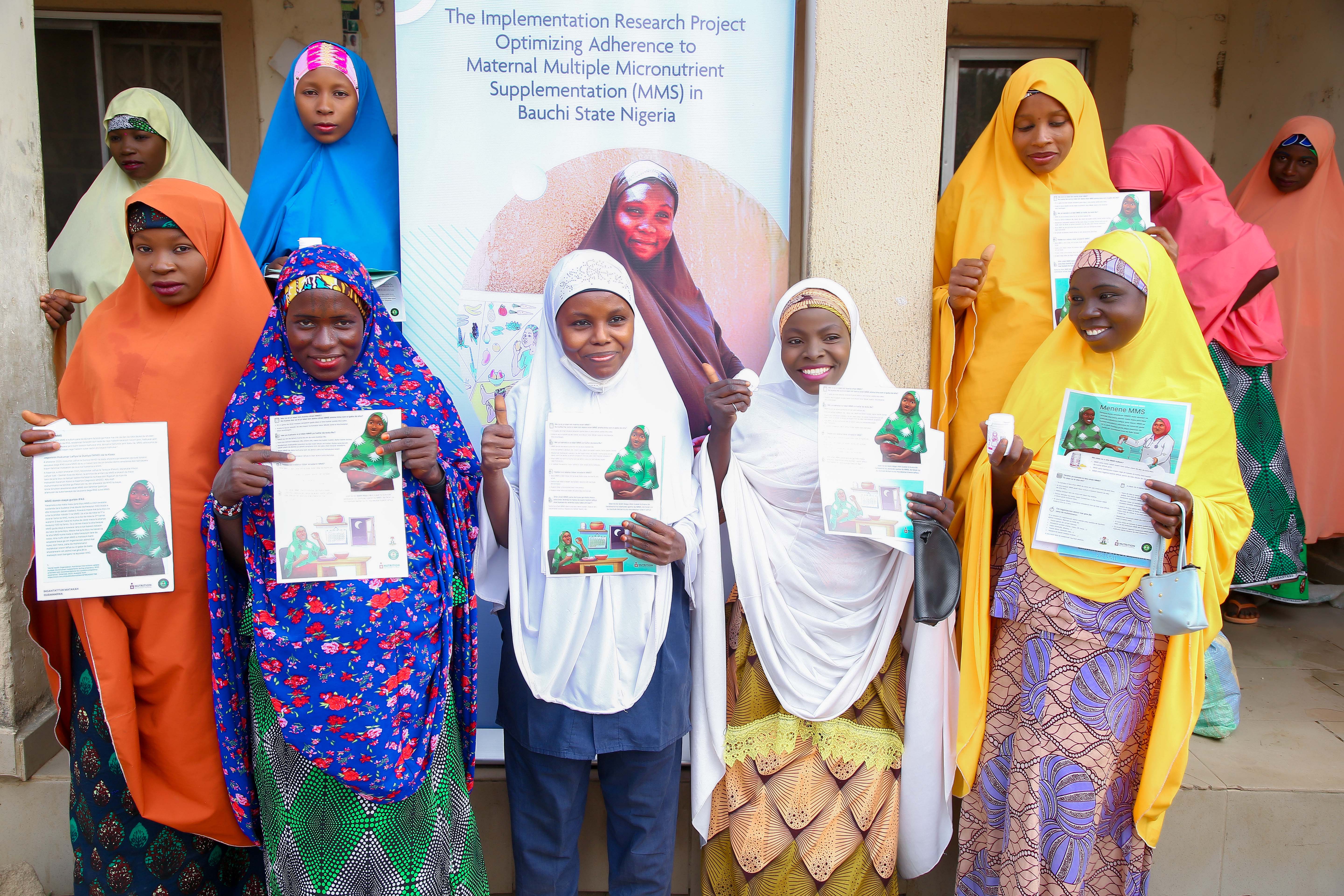 A group of women stand facing the camera holding a sheet of paper and supplement bottle.