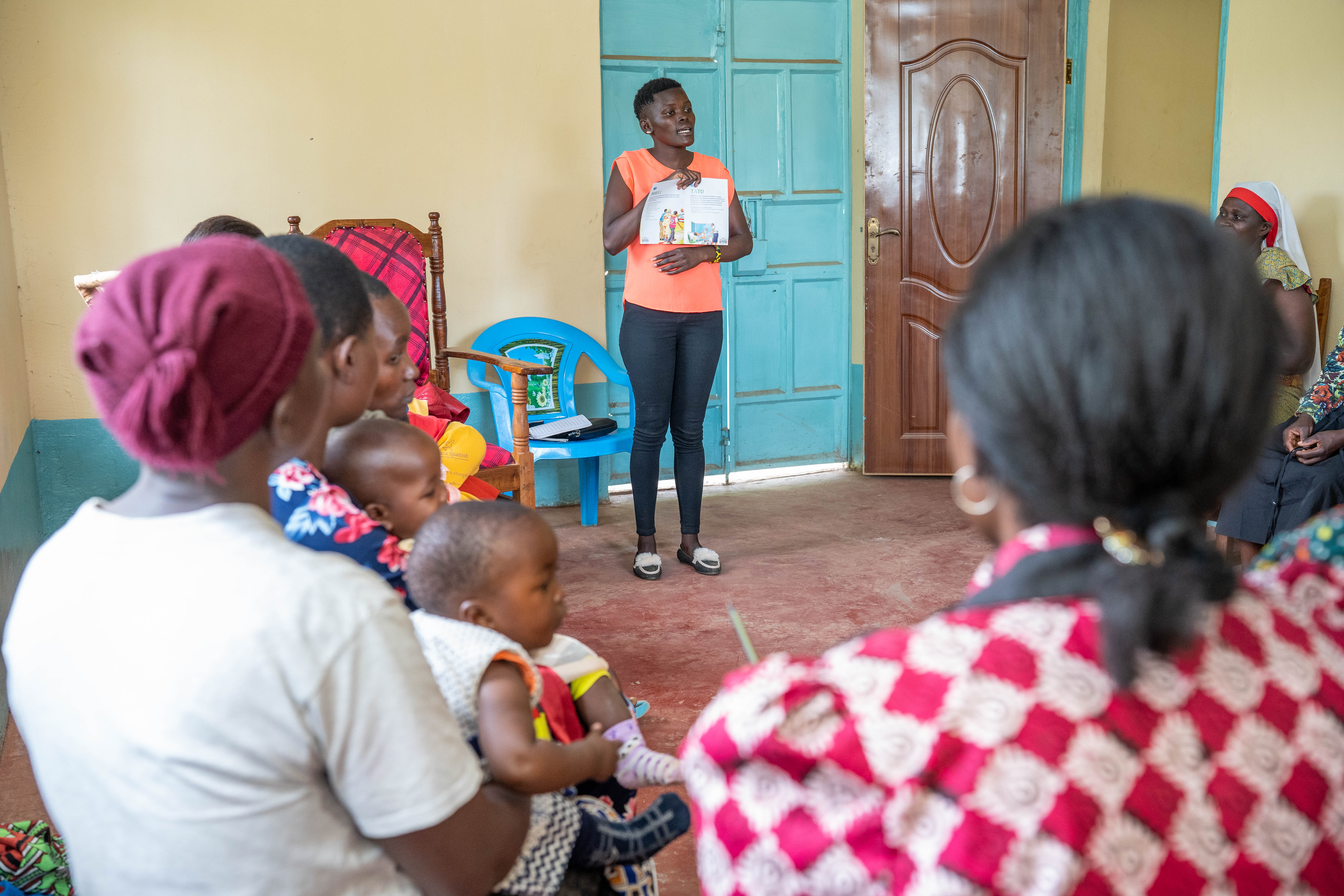 A woman holds up a booklet to teach a group of people.