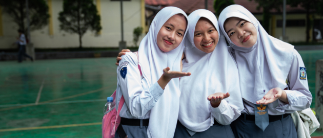 Three girls face the camera, smiling and blowing a kiss.