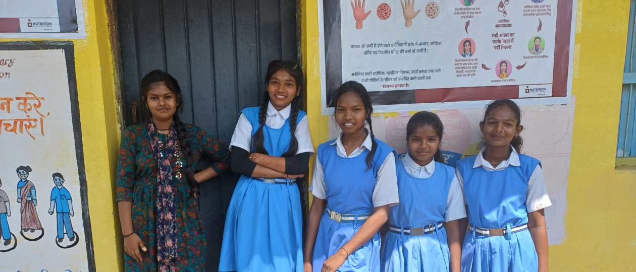 A group of students in their school uniforms stand outside smiling to the camera