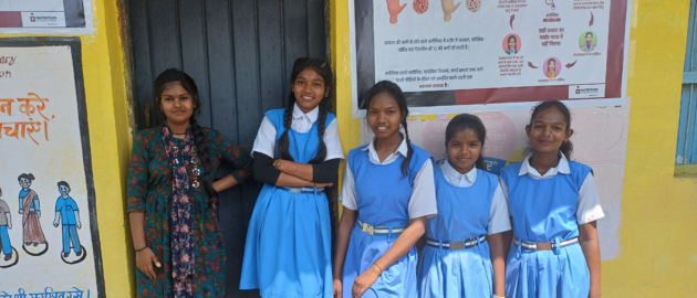 A group of students in their school uniforms stand outside smiling to the camera