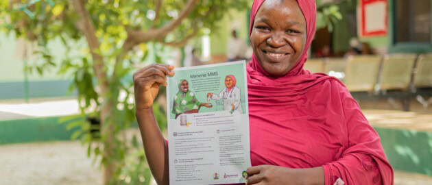 A woman hold a fact sheet on MMS in Nigeria and smiles at the camera.