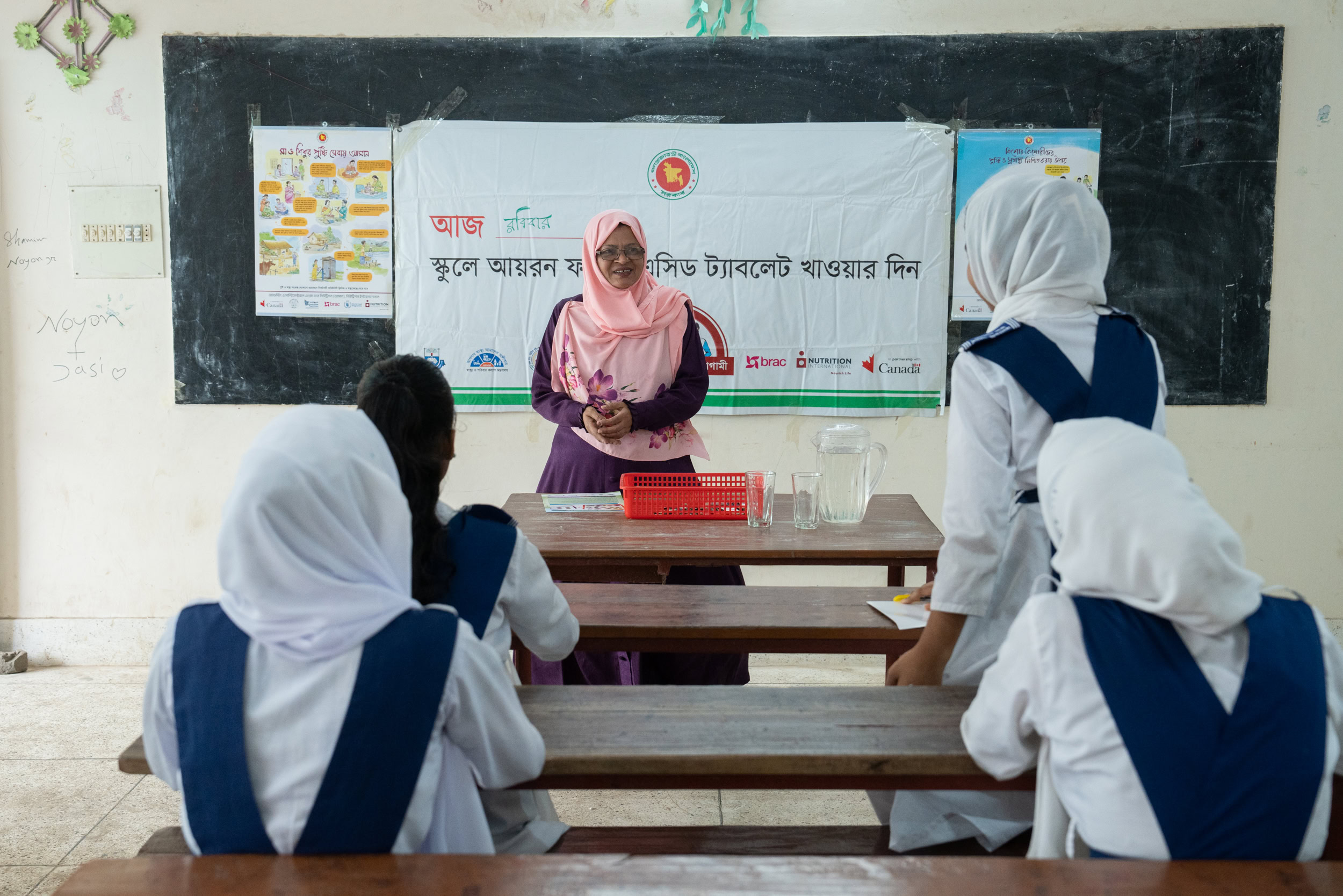 A teacher stands at the front of a classroom and listens as one student stands up and speaks.