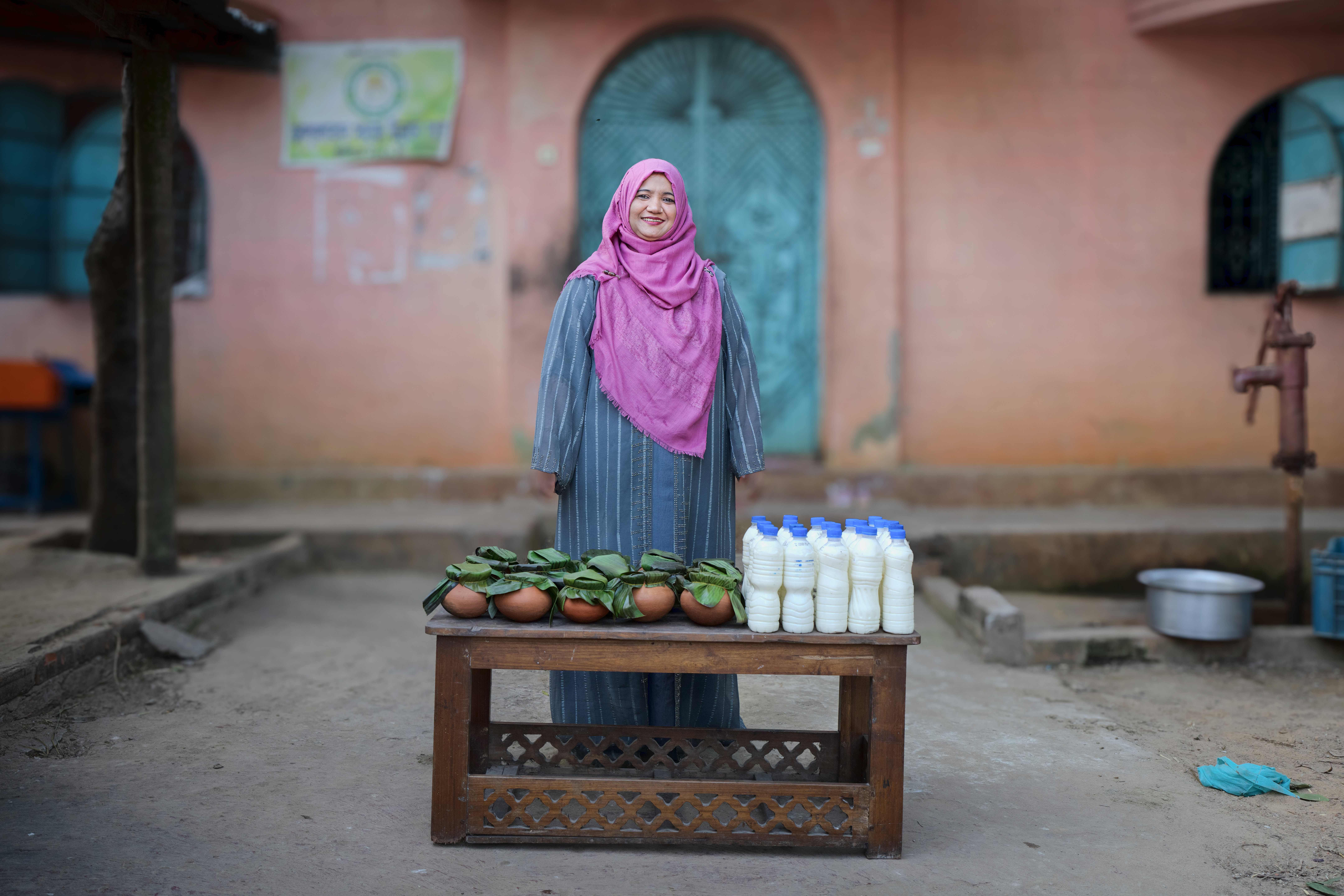 A woman stands behind a table prepared to sell many jars of milk.
