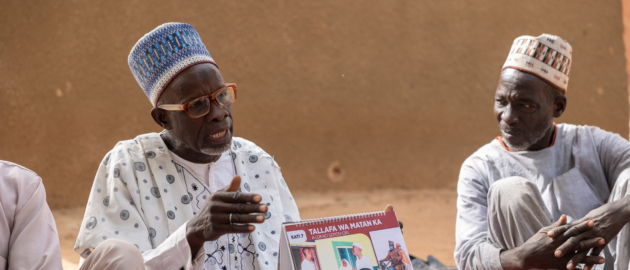 A man sits outside holding up a pamphlet promoting male involement in caregiving